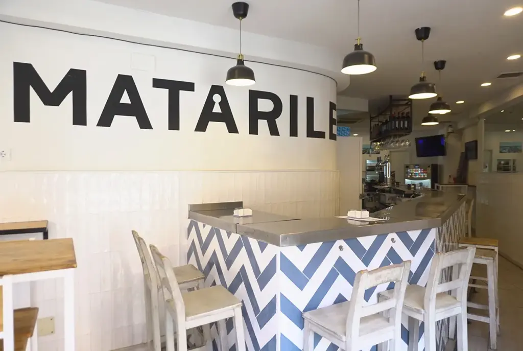 Detalle de la barra de diseño con taburetes y logo retroiluminado en el interior de Matarile Bar.