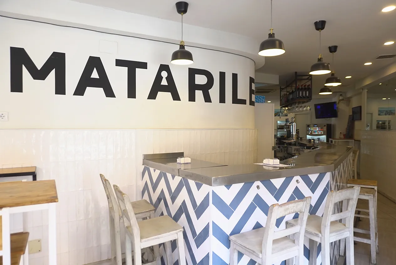 Detalle de la barra de diseño con taburetes y logo retroiluminado en el interior de Matarile Bar.